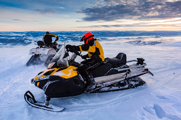 Two men are riding snowmobile in mountains.