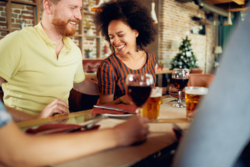 Friends chatting and drinking alcohol while  sitting at restaurant. Multi ethnic group.