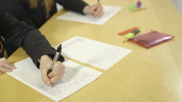 A tracking shot of two girls in a classroom or exam working and writing essays.
