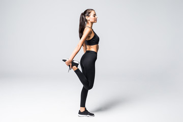Full length portrait of beautiful young woman doing stretching exercise isolated over gray background