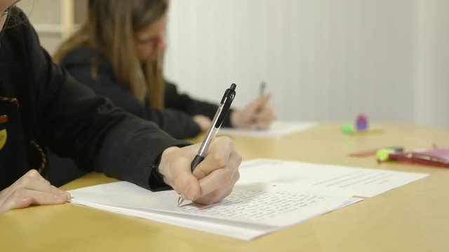 Tracking shot of two girls in school uniform writing in an exam in a school or college.