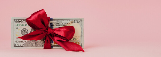 one hundred dollars gift wraped with a red ribbon on pink background