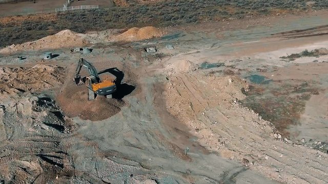 Aerial view of a backhoe working the ground at a construction site on the edge of town