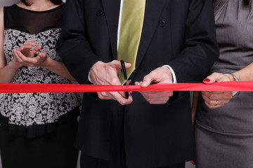 Businessman cutting red ribbon while other people next to him are clapping hands
