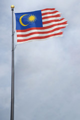 Worn and tattered Malaysia flag blowing in the wind on a cloudy day