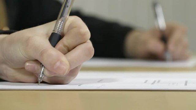 Close up of girls hands writing essays in an exam, classroom or exam hall.
