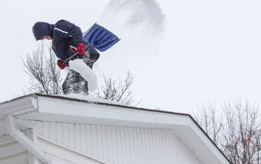 man on top of roof of house shovelling off snow