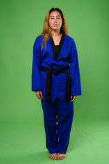 Young Asian woman wearing blue karate Gi against green backgroun