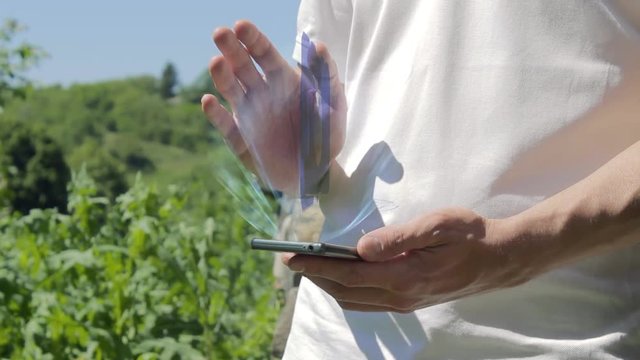 Man shows concept hologram apple on his phone. Person in white t-shirt with future technology holographic screen and green nature background