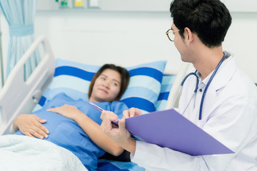 Fototapeta premium Asian young pregnant woman lying down talking and visit to her doctor man in a room.