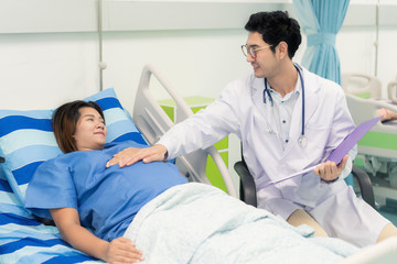 Asian young pregnant woman lying down talking and visit to her doctor man in a room.