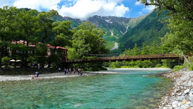 Tourists enjoying daytime around beautiful Kappa Bridge and turquoise Azusa river in sunny Kamikochi, surrounded by moving clouds near Mount Hotaka, Okuhotaka. 30fps RL pan motion timelapse footage