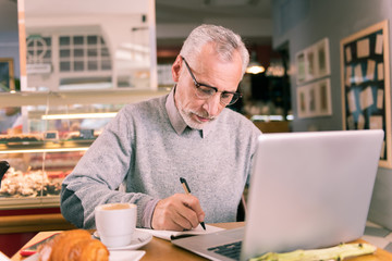 Writer in glasses. Grey-haired mature writer wearing glasses and grey sweater working using his laptop