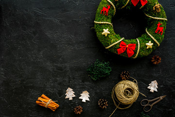 Christmas decoration concept. Traditional green christmas wreath near matherials and instruments, sciccors on black background top view copy space