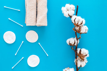 Cotton hygiene products. Cotton pads and swabs, towels twisted coil near dry cotton flowers on blue background top view