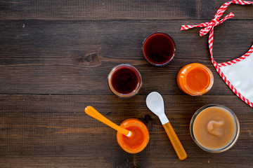 Set of baby puree with different flavors near bib on dark wooden background top view copy space