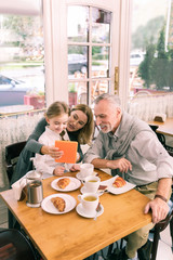 Beaming grandparents. Happy beaming grandparents eating morning croissants with cute little granddaughter