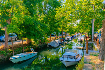 Obraz premium Canal and boats under trees in Lido of Venice, Italy