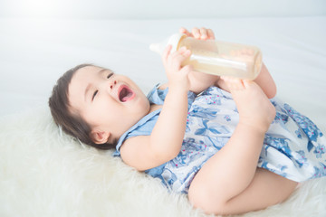 Little asian baby girl holding milk bottle and smiles on bed