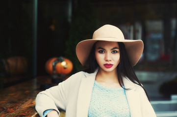 A young woman in a coat and a wide-brimmed hat on a city street .