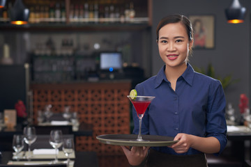 Portrait of pretty young Vietnamnese waitress bringing cocktail