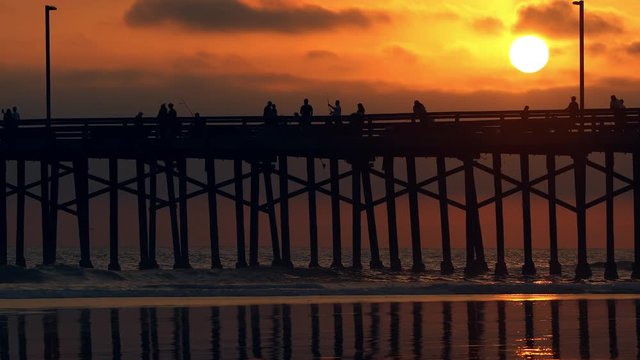People walking across pier during colorful sunset at Newport Beach.