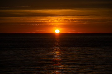 Fototapeta premium Large orange sunset as the massive sun sets into the horizon above the ocean, France