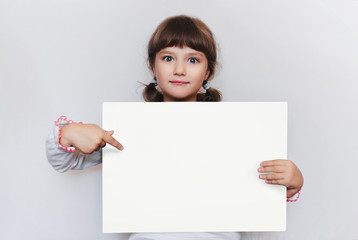 The little girl is holding a blank sheet of paper. Education. Advertising. Copy space. Point the finger at an empty space for text.