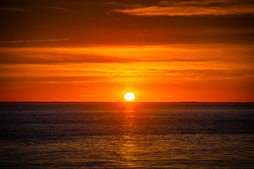Obraz premium Large orange sunset as the massive sun sets into the horizon above the ocean, France