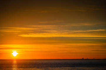Naklejka na ściany i meble Large orange sunset as the massive sun sets into the horizon above the ocean, France