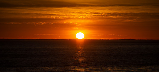 Fototapeta na wymiar Large orange sunset as the massive sun sets into the horizon above the ocean, France