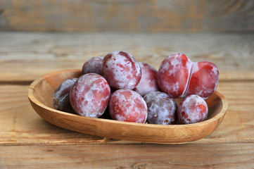 ripe plums in wooden plate on wooden background