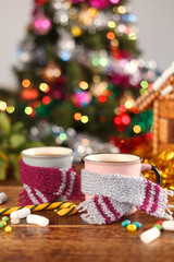 Cups in cozy scarves on the background of Christmas trees. New