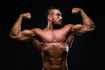 Fototapeta na wymiar Muscular fitness burnet beard man is showing biceps on black background