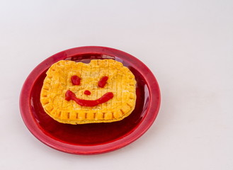 A pie with a friendly face drawn with tomato sauce isolated on a plate on a white background image with copy space in landscape format