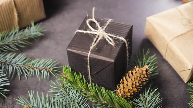 Black and brown paper christmas gift box with pine branches on dark texture surface.