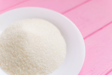 Sugar on a white plate on a wooden pink background.