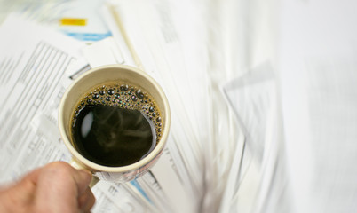 Deadline written on paper and a cup of coffee in hand against a background of scattered papers.