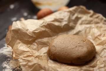 Ready dough for Christmas cookies with cinnamon, ginger and sugar. On parchment. On a dark brown background sprinkle with flour. New year's magic. With the blur