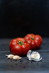Two ripe red juicy tomatoes with spices. Garlic, black pepper peas. Shot in a low key, on a dark background.