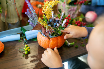 a child makes a flower arrangement in a pumpkin on the table