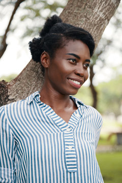 Smiling beautiful young Black woman standing inter teen in park and looking away