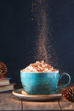 Hot chocolate with cream and cinnamon stick in a blue ceramic cup on a table with a books. The concept of winter or fall time.