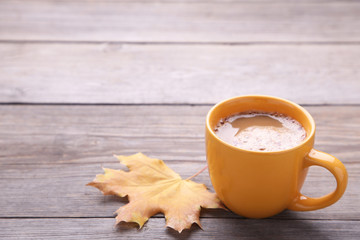 Cup of coffee with dry autumn leaf on wooden background