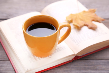 Cup of coffee with autumn leaf and book on wooden background