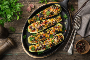 Stuffed zucchini boats with vegetables ( tomato, pepper, corn, red onion and olives) and cheese in cast iron pan