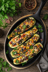 Stuffed zucchini boats with vegetables ( tomato, pepper, corn, red onion and olives) and cheese in cast iron pan