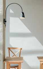 Wooden chair stool and wooden table on white wall background and black modern wall lamp in a cafe with sunlight shade