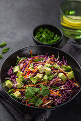 healthy rainbow cole slow, red cabbage, avocado, carrot and bell pepper salad in black bowl