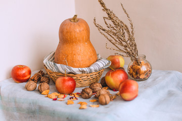 Still life with cinnamon sticks wrapped in twine, apples, pumpkin in a wicker basket stand on a striped linen cloth, walnuts and flower petals in bank. Concept of home comfort in autumn or wint